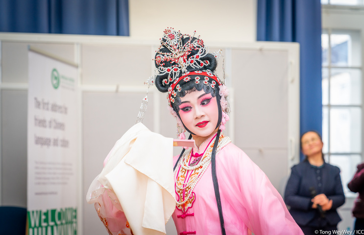 Bild einer Frau in einem weißen und rosa Kostüm für die Peking-Oper mit Haarschmuck, weiß und blassrosa geschminktes Gesicht.