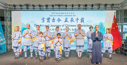 Eine Kampfkunsttruppe steht in Zweierreihe mit Ihrem Kampfkunstlehrer für ein Gruppenphot Model. Die Kampfkünstler*innen sind gekleidet in Chinesicher Kampfkunstkleidung in sanftem Blau mit goldenen Scherpen. Der Kampfkunstlehrer hebt sich ab durch eine Robe in dunklerem Blau. Im Hintergrund ein großes Banner und am Rechten Rand die Rote Flagge der Volksrepublik.